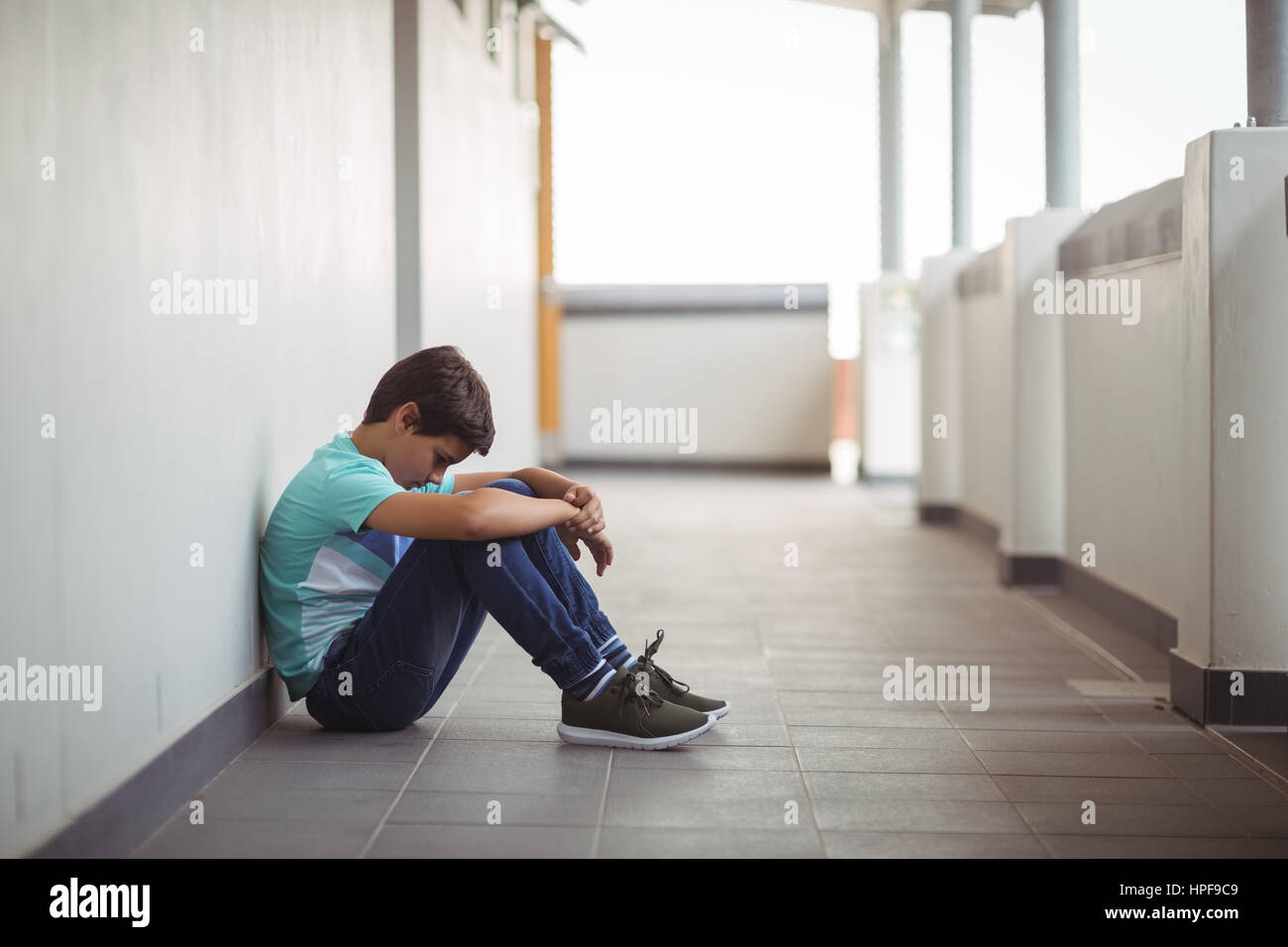 Sad schoolboy sitting in corridor of school Stock Photo - Alamy