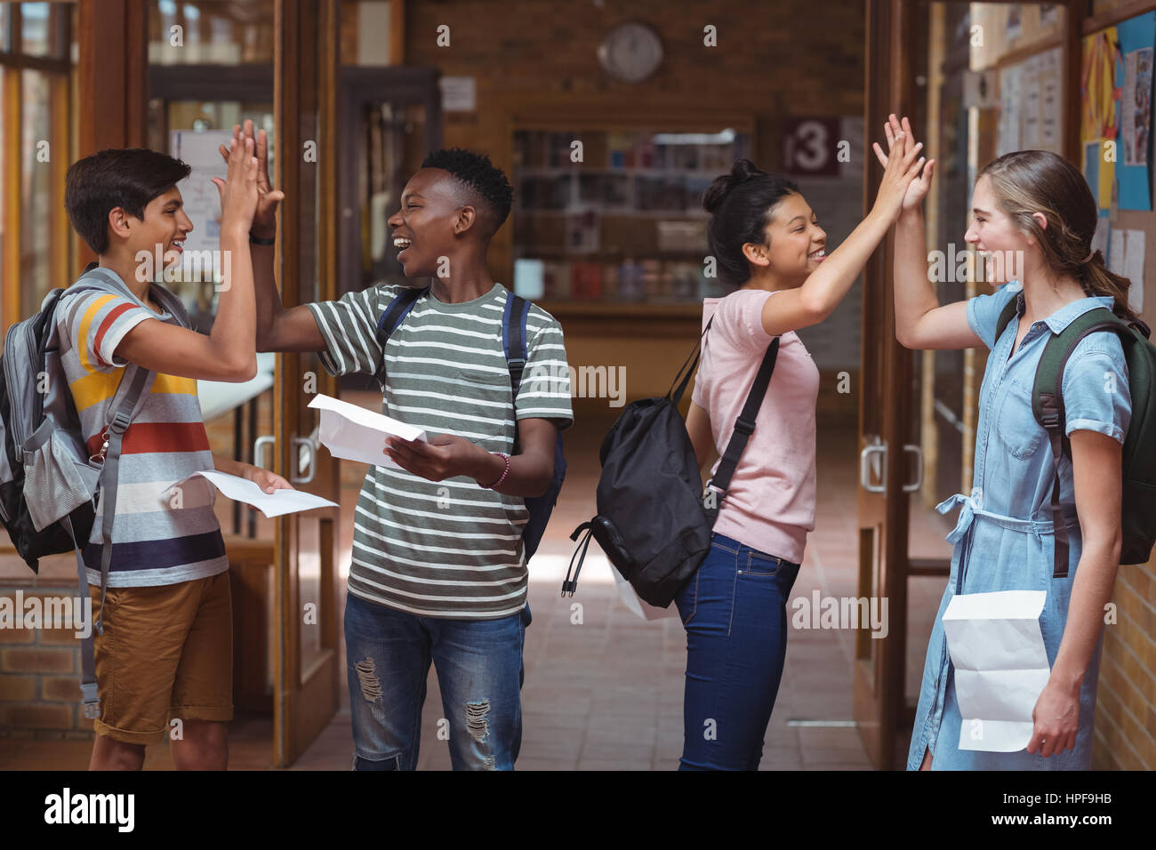 Happy classmates giving high five to each other in corridor at school ...