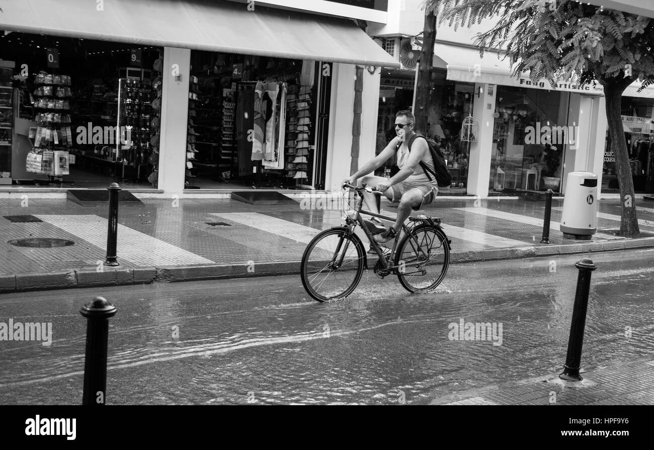 Couple having a ride by bike, in a rainy day, in the tiny touristic village of Cala d´or, mallorca... the streets are not preapared for such big rain. Stock Photo