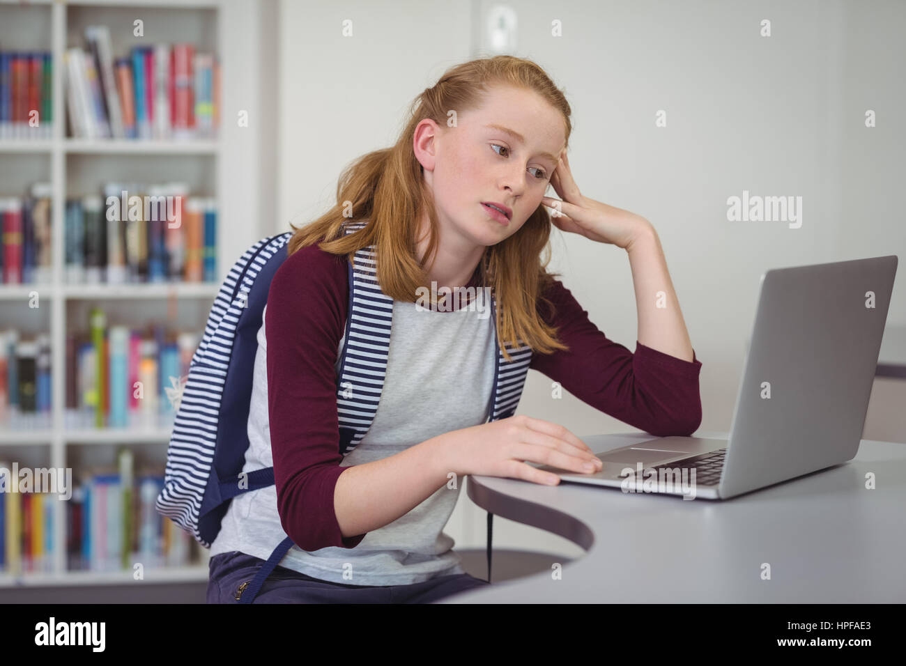Thoughtful schoolgirl using laptop in library at school Stock Photo - Alamy