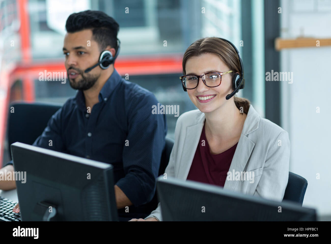 Smiling business executives with headsets using computers at desk in ...