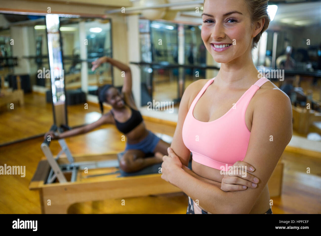 Portrait of smiling fit woman standing with arms crossed in fitness ...