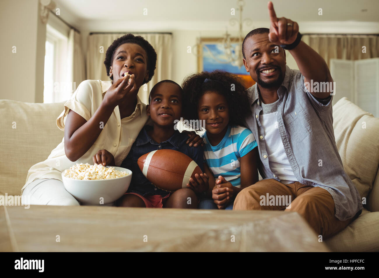 Parents and kids having fun while watching television in living room at home Stock Photo
