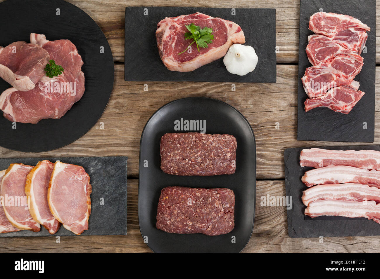 Varieties of meat on black tray against wooden background Stock Photo