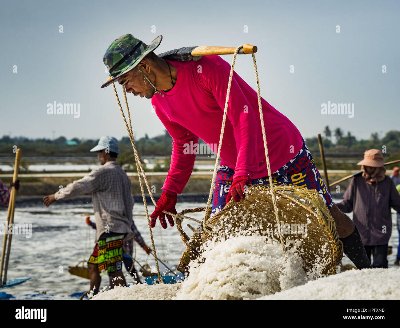 Bang Kaeo, Petchaburi, Thailand. 22nd Feb, 2017. A worker unloads baskets of salt during the salt harvest in Petchaburi province of Thailand, about two hours south of Bangkok on the Gulf of Siam. Salt is collected in coastal flats that are flooded with sea water. The water evaporates and leaves the salt in large pans. Coastal provinces south of Bangkok used to be dotted with salt farms, but industrial development has pushed the salt farms down to remote parts of Petchaburi province. The harvest normally starts in early February and lasts until early May, but this year's harvest was delaye Stock Photo