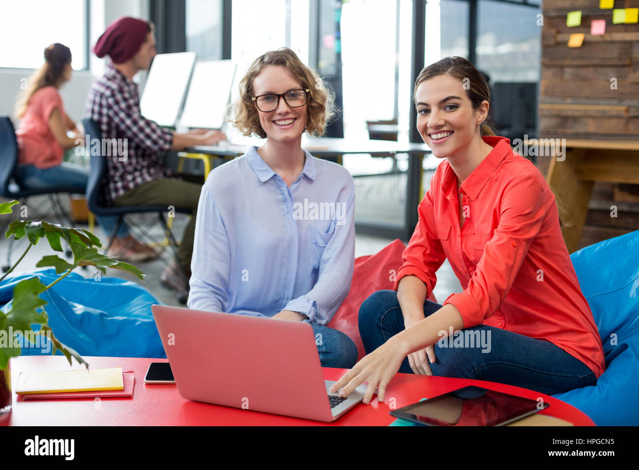 Portrait of smiling business executives sitting in office with laptop ...