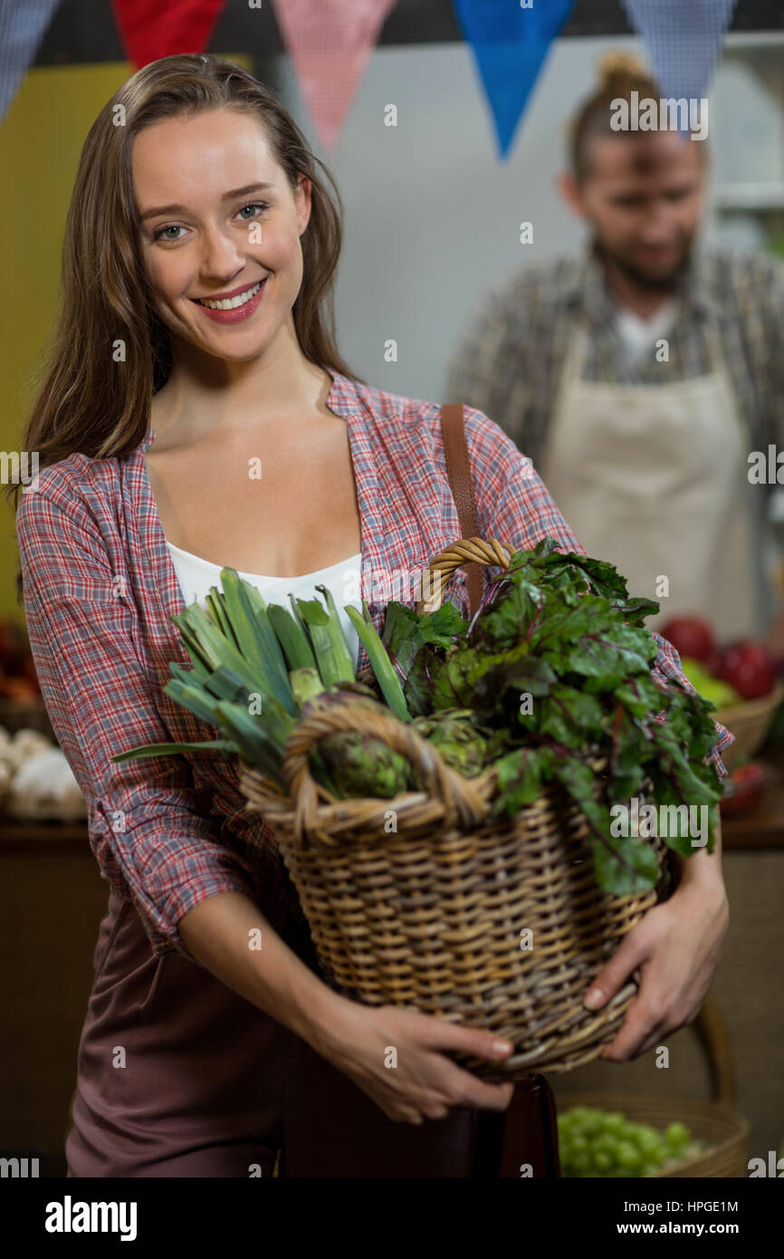Portrait of smiling woman holding basket of green leafy vegetables in ...