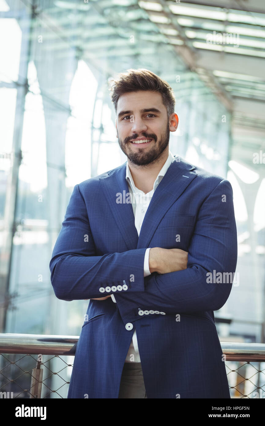 Portrait of businessman standing with arms crossed at railway station ...