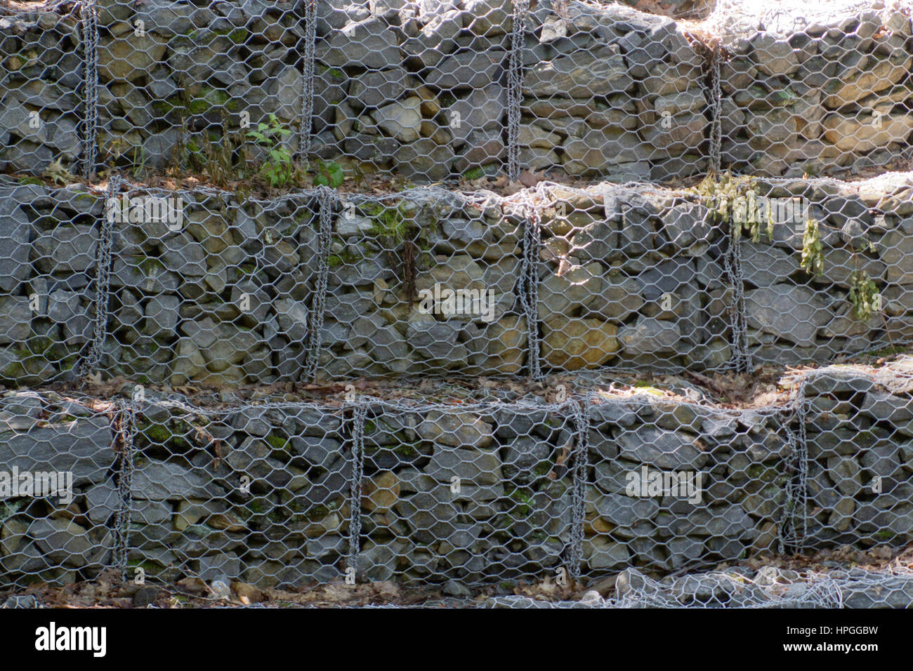 Tiers of screened in Gabion riprap (rock) line a stream to control river bank erosion and flooding Stock Photo