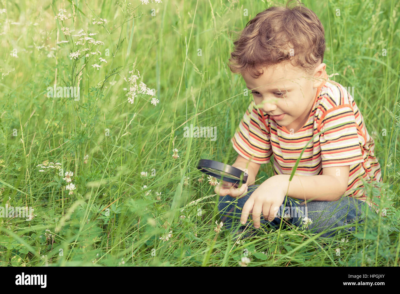 Happy little boy exploring nature with magnifying glass at the day time ...