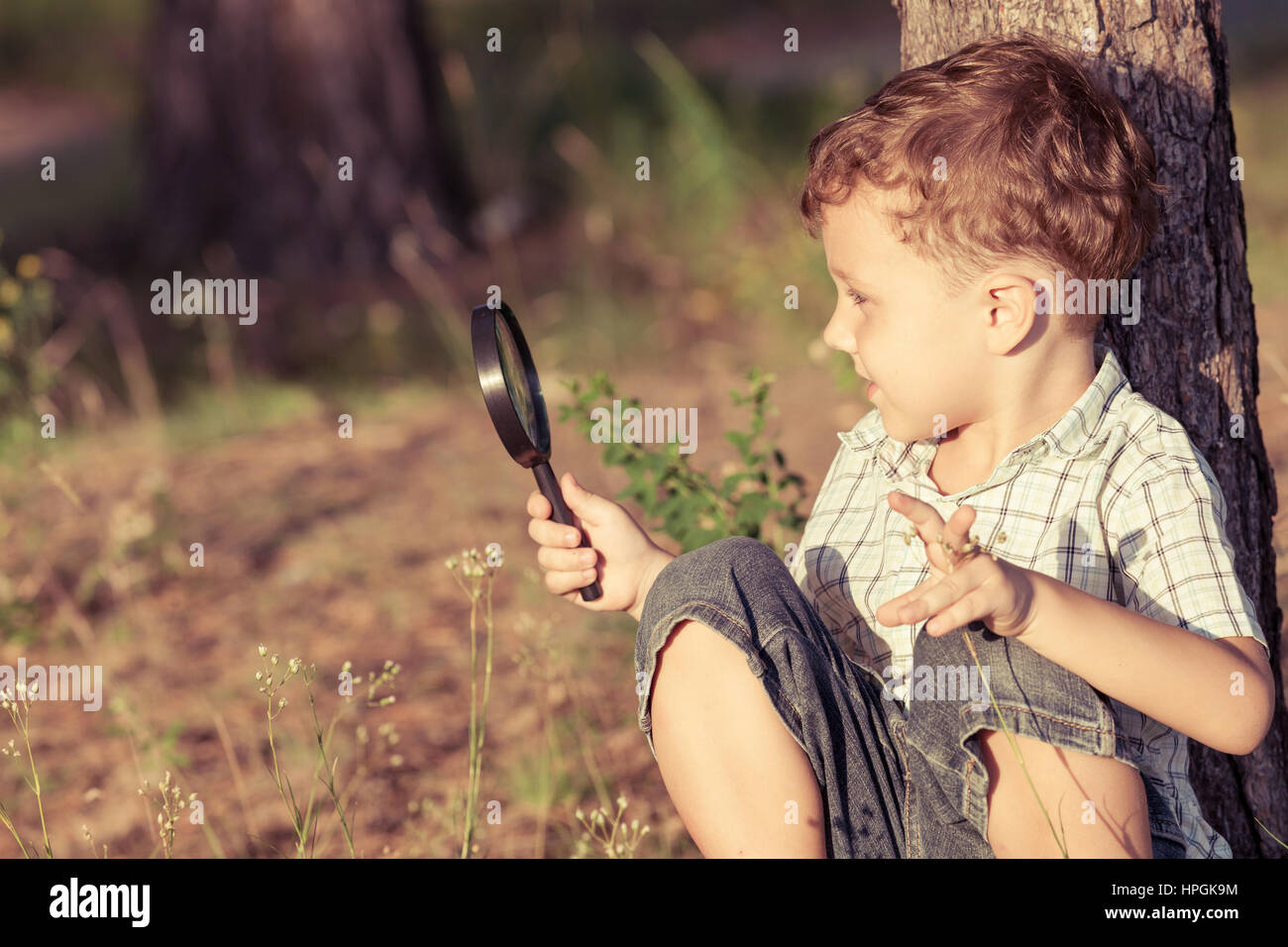 Happy little boy exploring nature with magnifying glass at the day time ...
