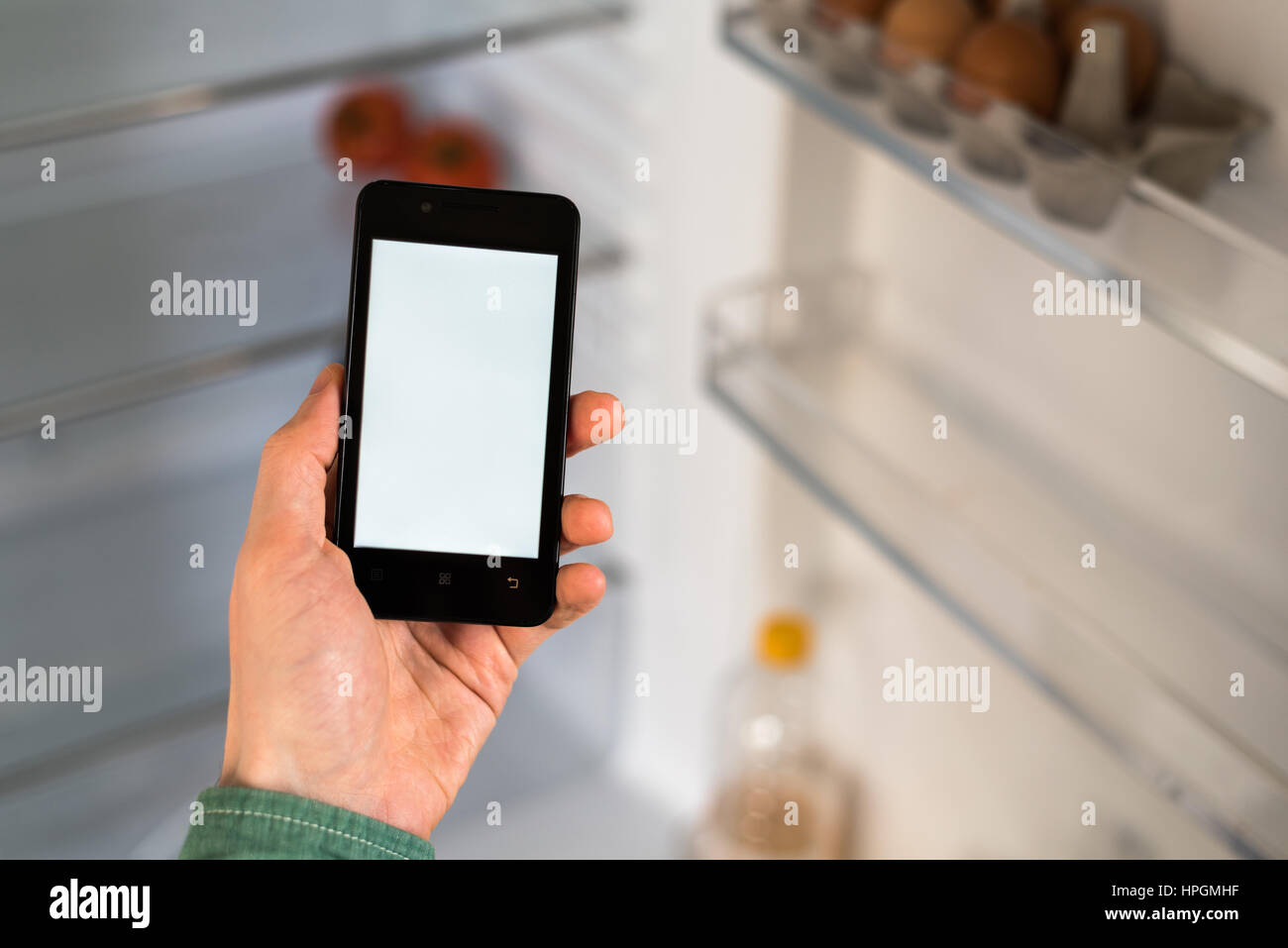 Close-up of person hands holding smartphone showing white screen on display. Empty Refrigerator on background Stock Photo