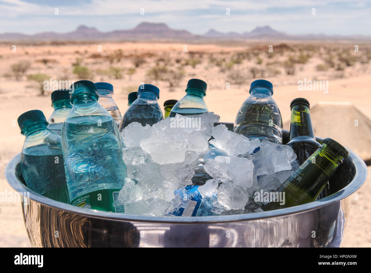 Bottles of water and beer in a stainless steel bowl with ice to keep them cool.  Pictured on a hot summer's day Doro Nawas Camp, Damaraland, Namibia. Stock Photo