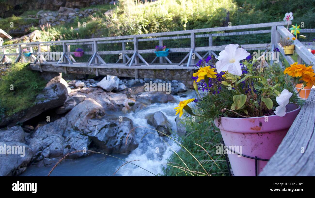 Traditional wooden footbridge with flower pots crossing rocky river