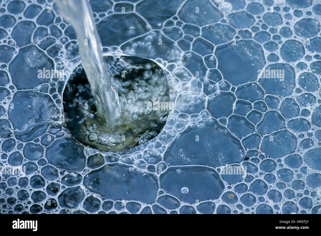 Water feature in a garden pond cascading water through a hole in the ice with bubbles forming underneath Stock Photo