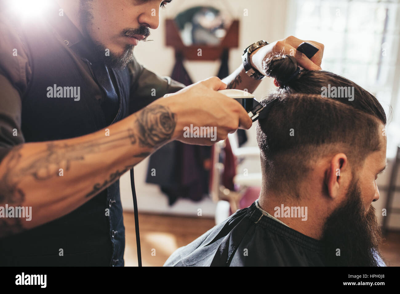 Close up shot of man getting trendy haircut at barber shop. Male hairstylist serving client, making haircut using machine and comb. Stock Photo
