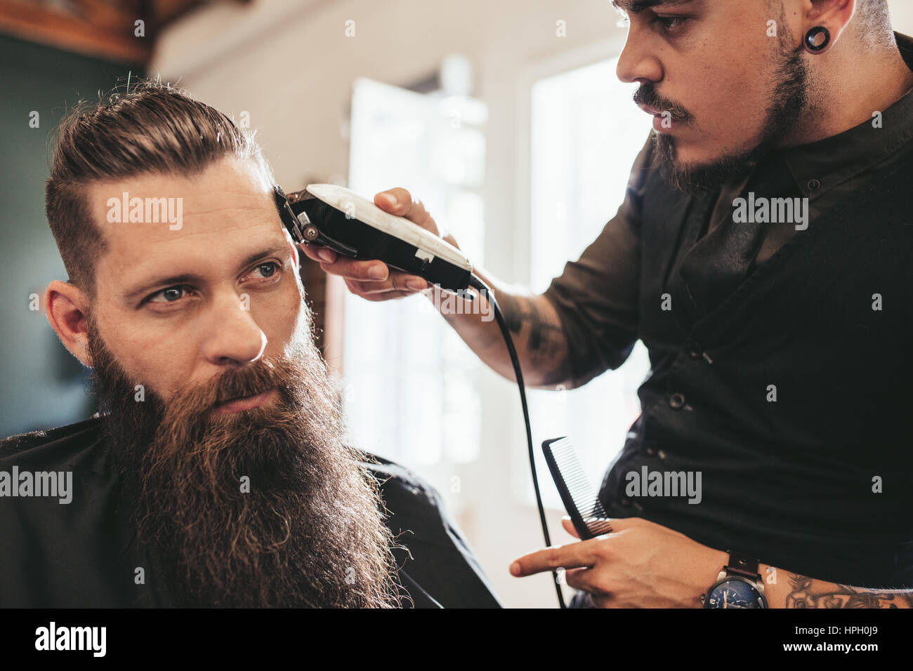 Young man getting trendy haircut at salon. Hairstylist giving stylish haircut to client at barber shop. Stock Photo