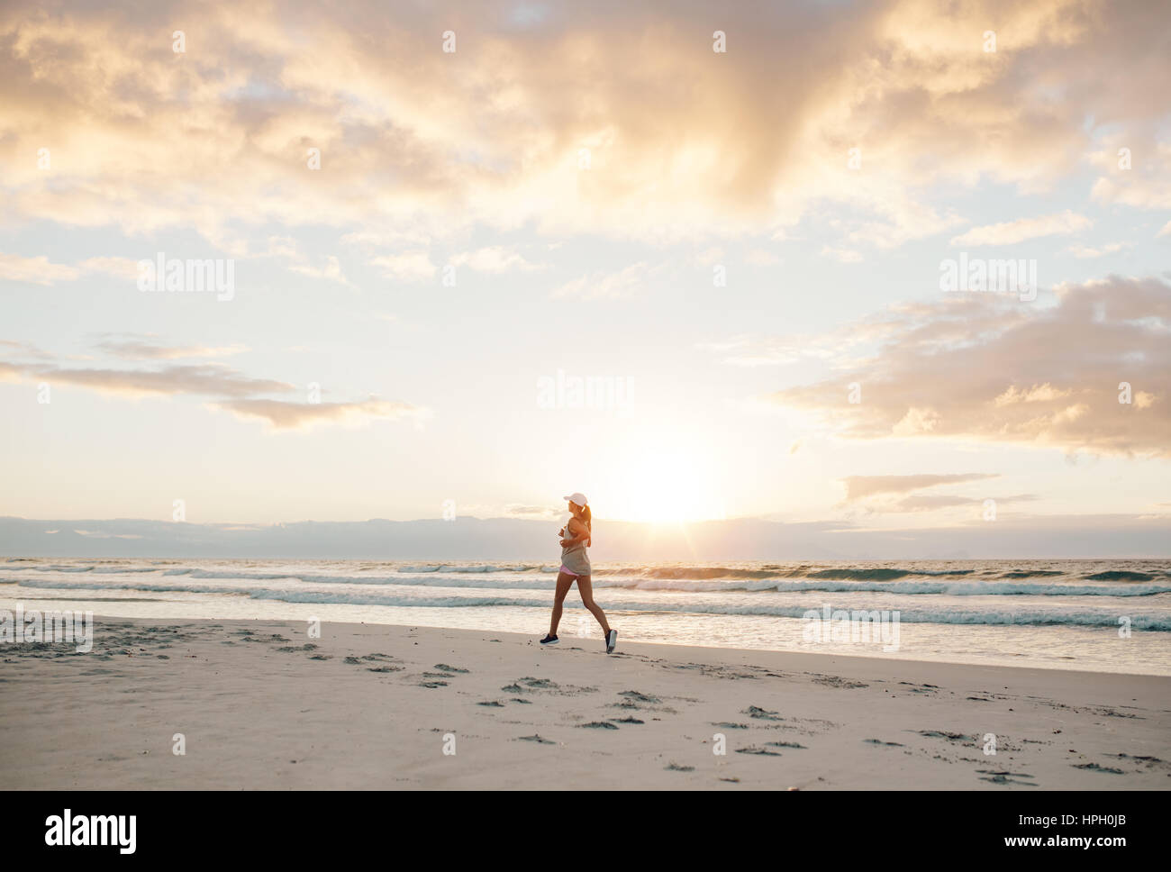 Shot of fitness woman running along the beach in morning. Healthy female jogging on the sea shore. Stock Photo