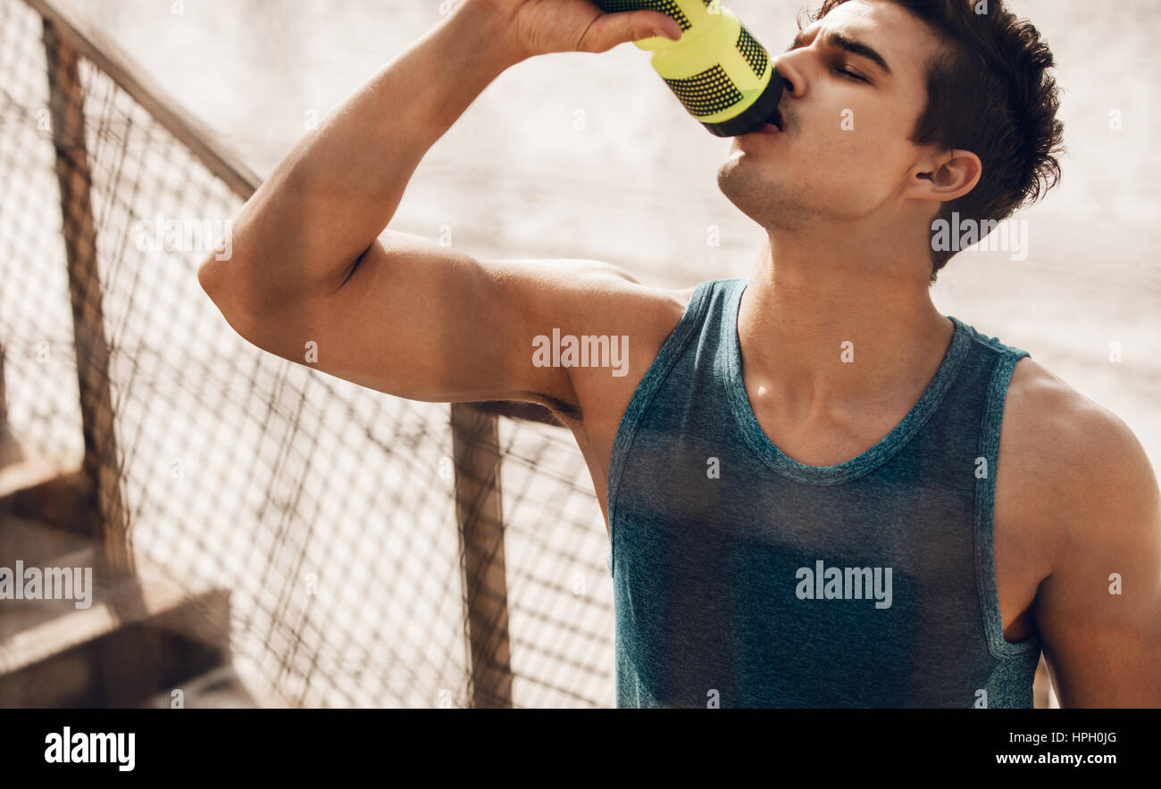 Man drinking water after running workout at beach. Thirsty healthy male with fit body drinking water. Stock Photo