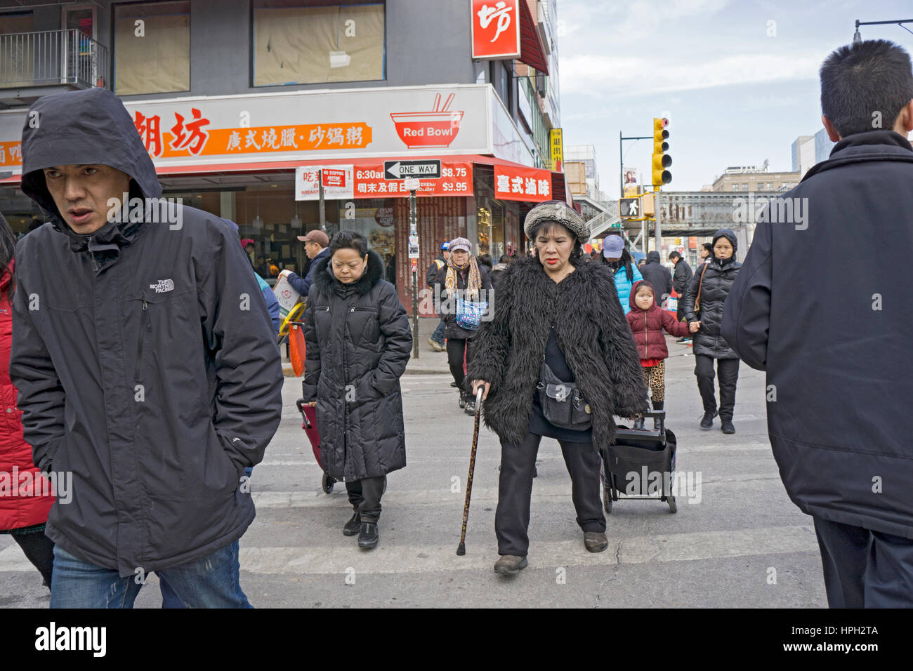 An Asian woman with a cane wearing contemporary clothes crossing a street in Chinatown, Flushing, New York City Stock Photo