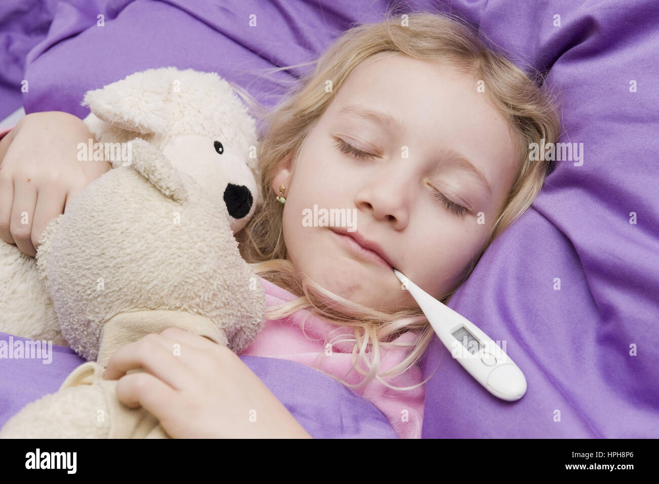 Krankes Maedchen liegt mit Fieberthermometer im Bett - sick girl with clinical thermometer in bed, Model released Stock Photo