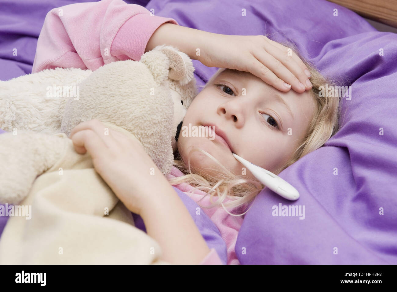 Krankes Maedchen liegt mit Fieberthermometer im Bett - sick girl with clinical thermometer in bed, Model released Stock Photo