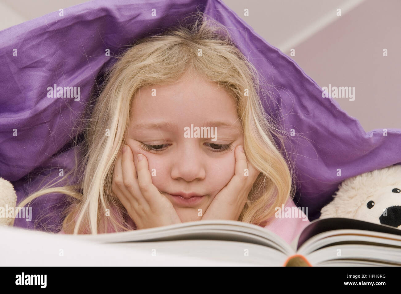 Maedchen liegt unter der Bettdecke und liest ein Buch - girl lying under bed cover reading a book, Model released Stock Photo