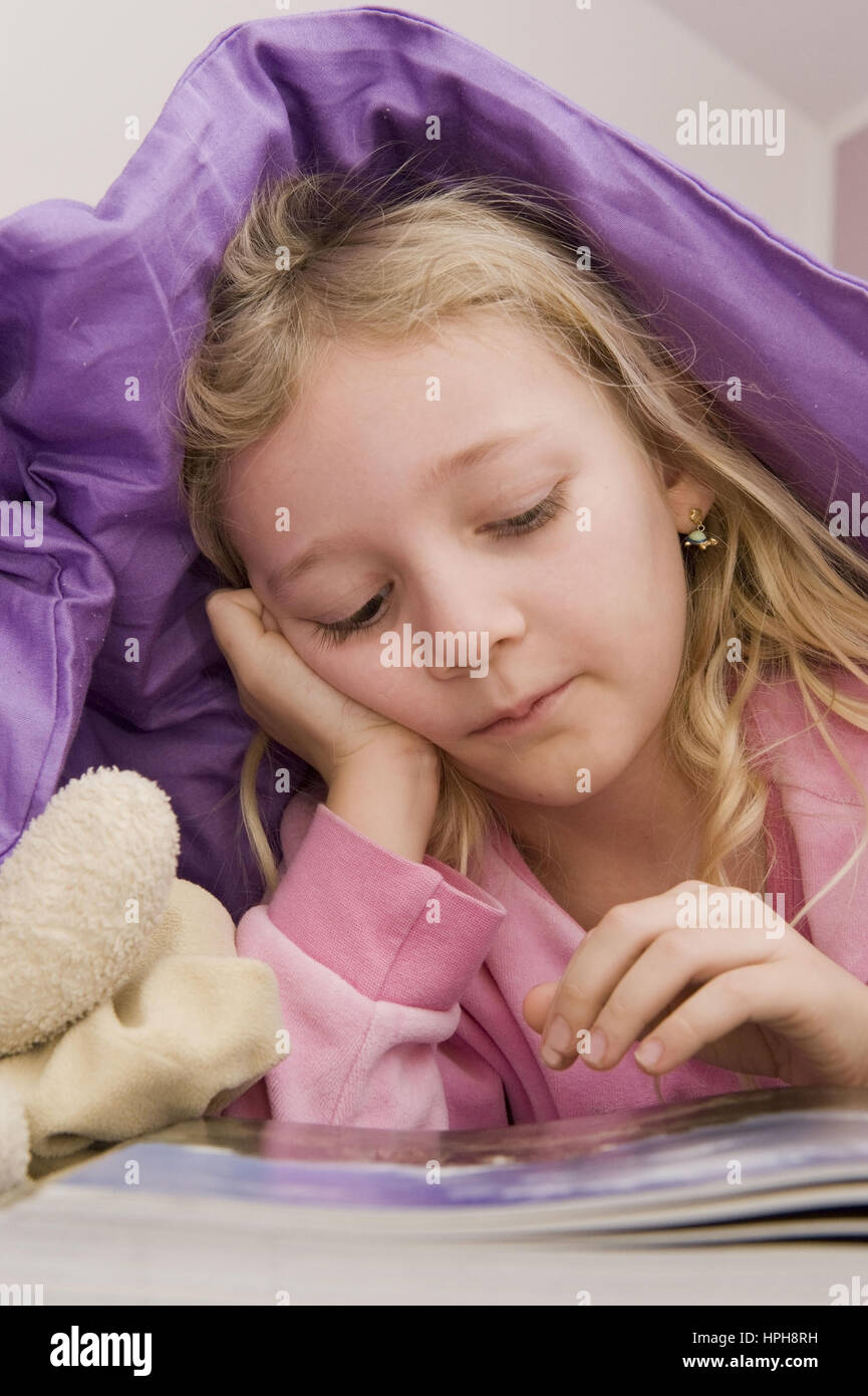 Maedchen liegt unter der Bettdecke und liest ein Buch - girl lying under bed cover reading a book, Model released Stock Photo