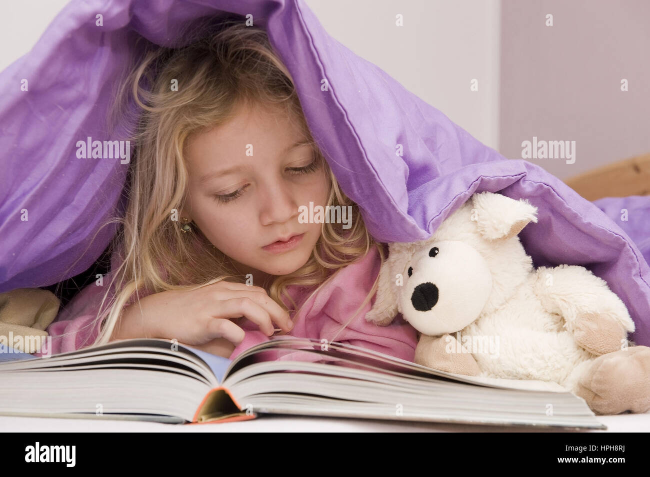 Maedchen liegt unter der Bettdecke und liest ein Buch - girl lying under bed cover reading a book, Model released Stock Photo