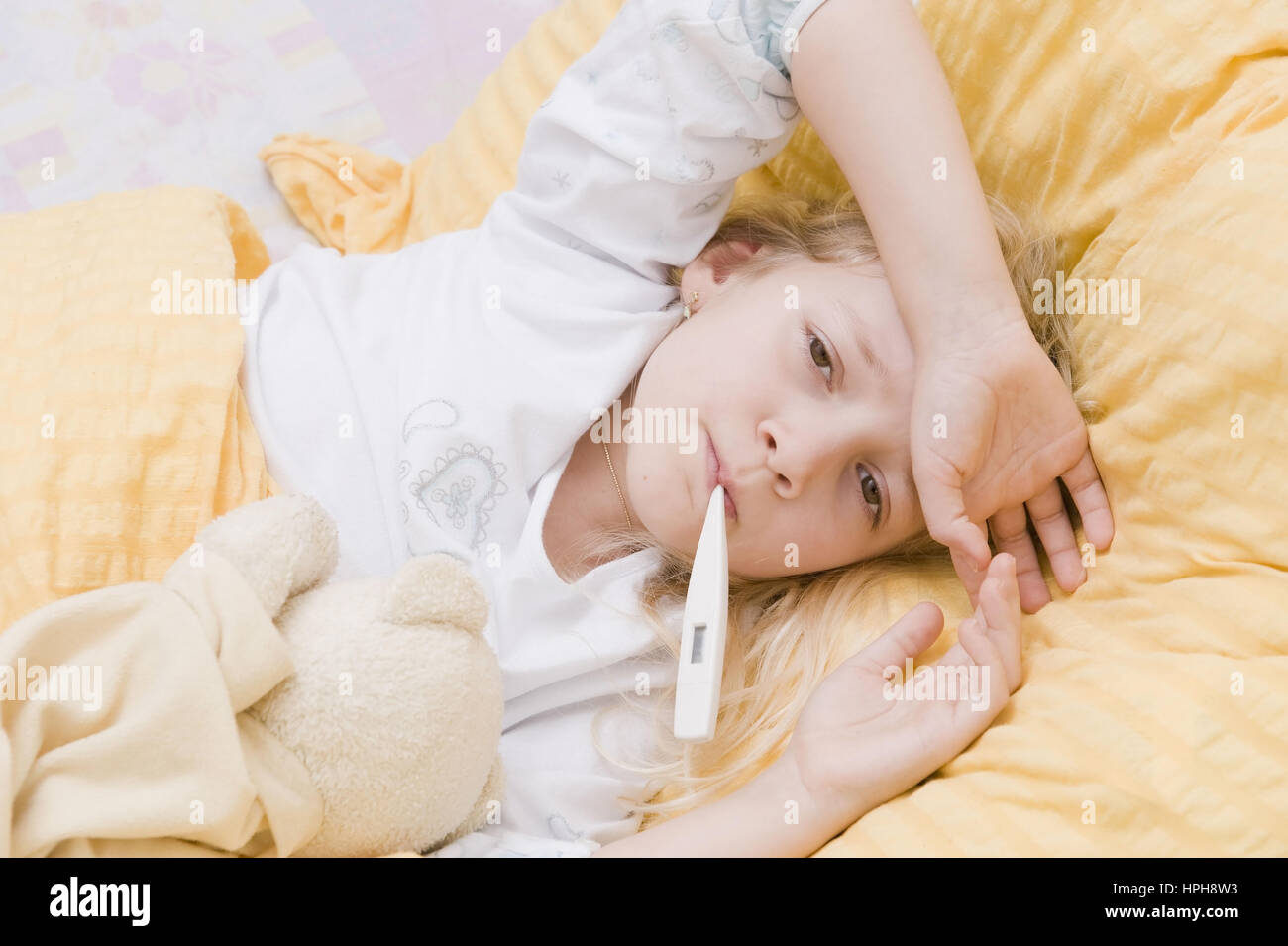 Krankes Maedchen liegt mit Fieberthermometer im Bett - sick girl with clinical thermometer in bed, Model released Stock Photo