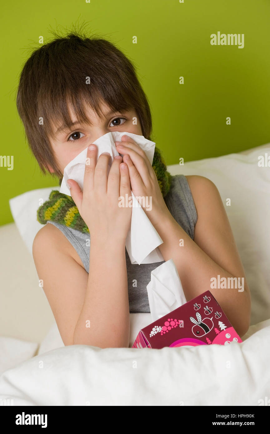 Kranker Junge schneuzt sich im Bett - sick boy in bed blows his nose, Model released Stock Photo