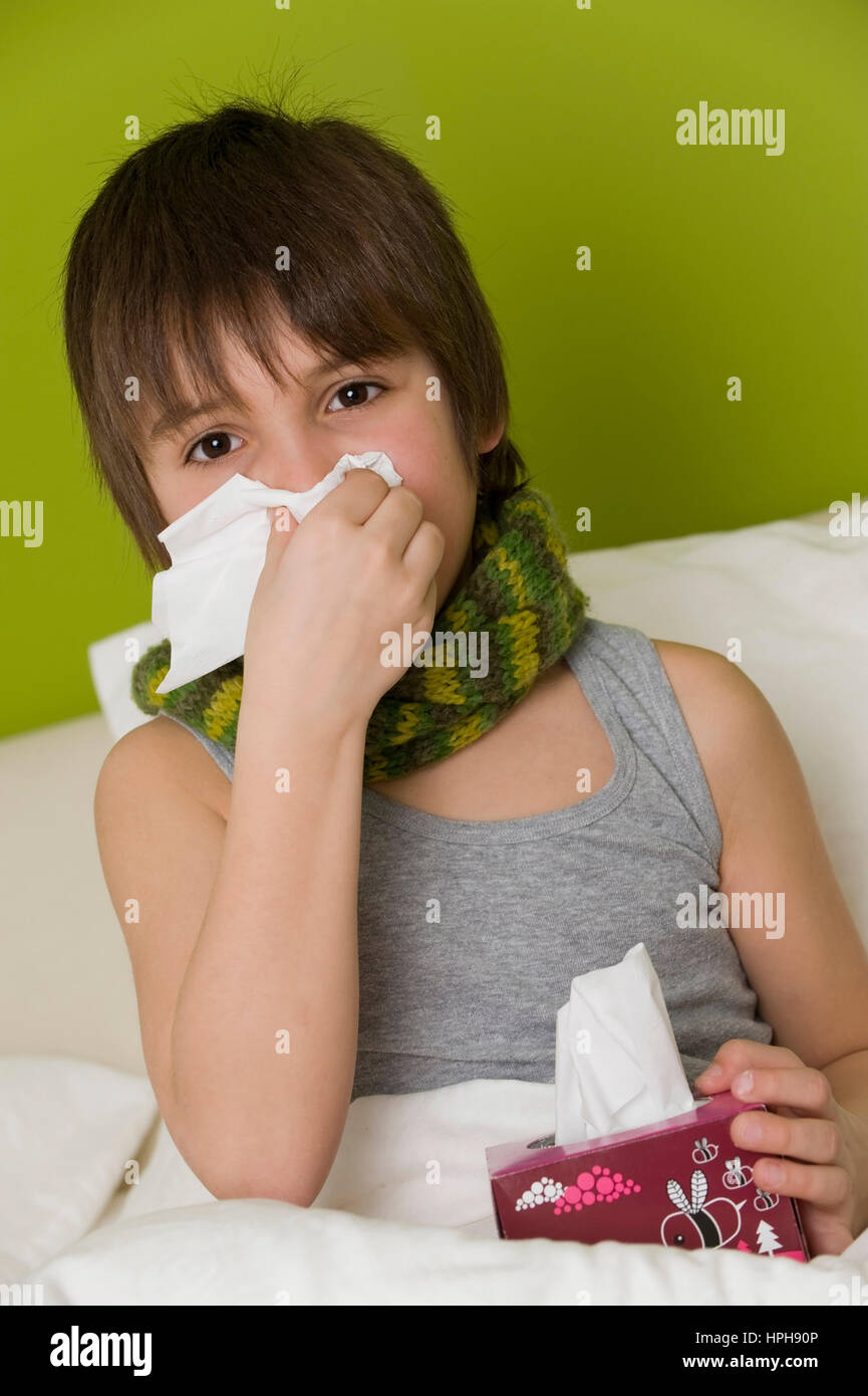 Kranker Junge schneuzt sich im Bett - sick boy in bed blows his nose, Model released Stock Photo