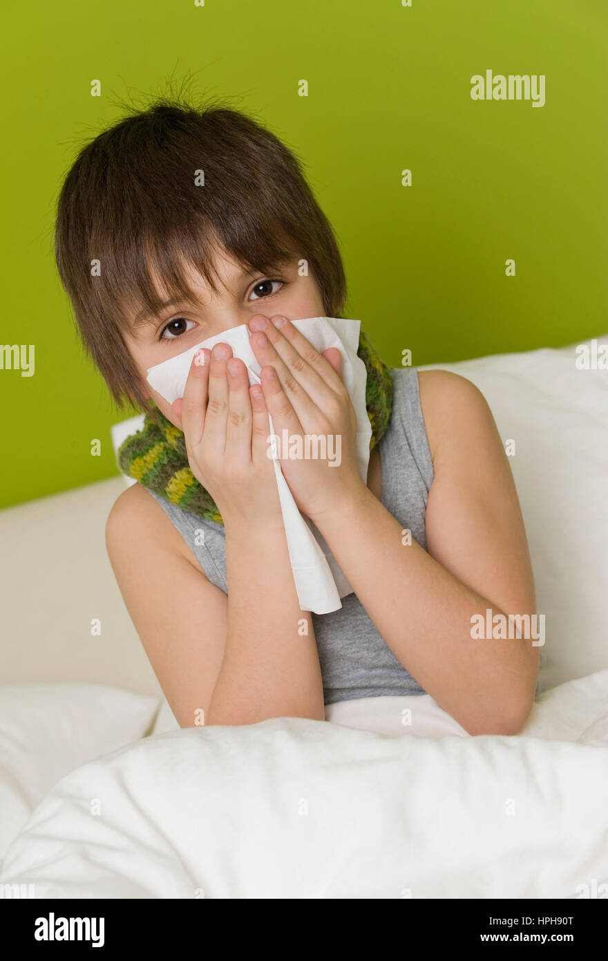 Kranker Junge schneuzt sich im Bett - sick boy in bed blows his nose, Model released Stock Photo