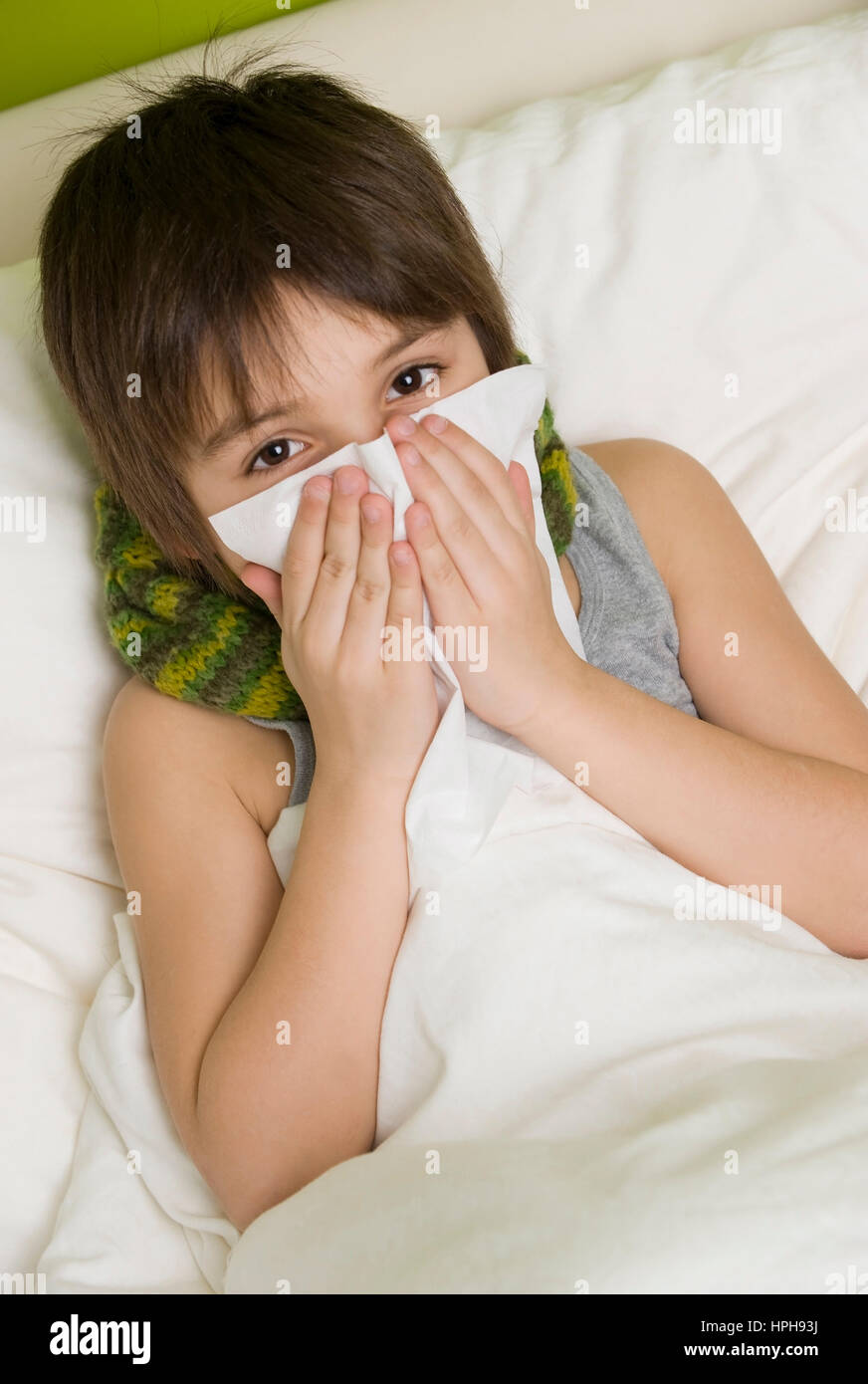 Kranker Junge schneuzt sich im Bett - sick boy in bed blows his nose, Model released Stock Photo