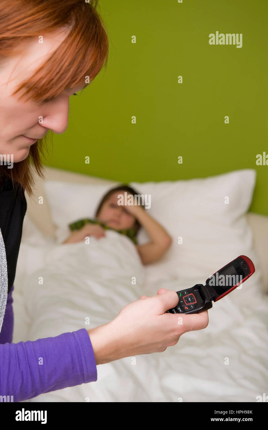 Krankes Kind liegt im Bett, Mutter ruft den Arzt an - child in bed, mother calls the doctor, Model released Stock Photo
