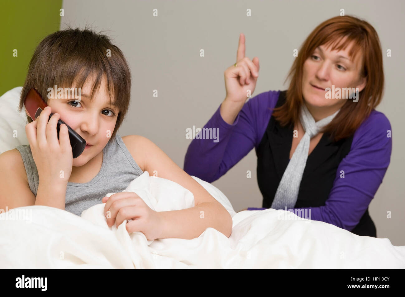 Sohn im Bett mit Handy, Mutter schimpft - son with mobile phone in bed, mother scolds, Model released Stock Photo