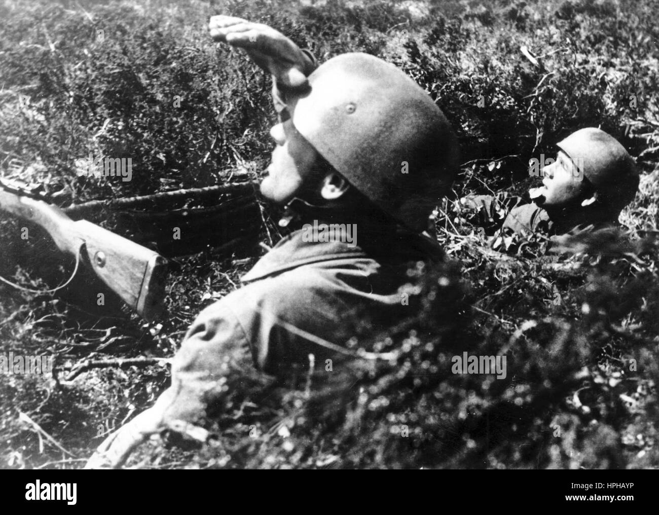 The Nazi propaganda image shows a German Wehrmacht paratrooper watching the skies in a camouflaged base on the Atlantic Wall. Published in June 1944. A Nazi reporter has written on the reverse of the picture, 'Paratrooper on the Atlantic Wall. Camouflaged until the last! In the hidden pockets of resistance and fortifications of the coasts, our paratroopers keep watch. In these 'invisible' field positions, every single man is totally camouflaged. Enemy reconnaissance is being watched by our paratroopers, as they unsuccessfully attempt to make out our positions.' Fotoarchiv für Zeitgeschichte Stock Photo