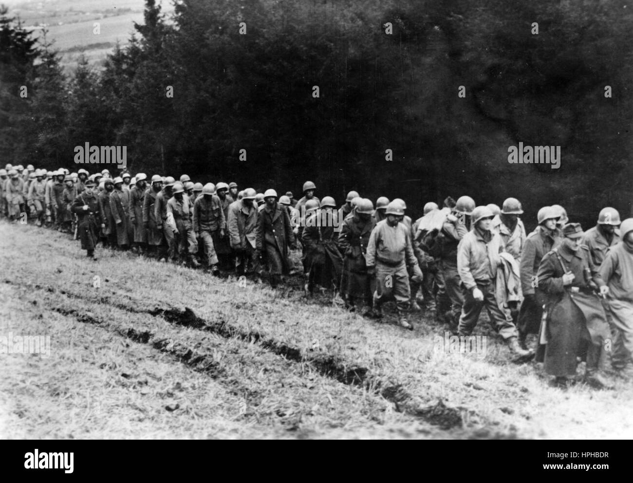 The Nazi propaganda image shows US-American soldiers after being taken prisoner by the German Wehrmacht on the Western Front. Published in December 1944. A Nazi reporter has written on the reverse of the picture on 28.12.1944, 'Prisoners from the Western Offensive being brought in. Between the Hohe Venn and the Northern part of Luxembourg, strong German forces have been on the offensive since 16.12.1944 and have overwhelmed North American bases. Already in the first few days, our troops have made thousands of prisoners carry out the march to German soil, quite contrary to what they would have  Stock Photo