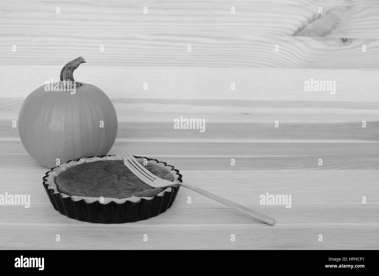 Fork with a small pumpkin pie on a wooden table with small gourd, with copy space Stock Photo