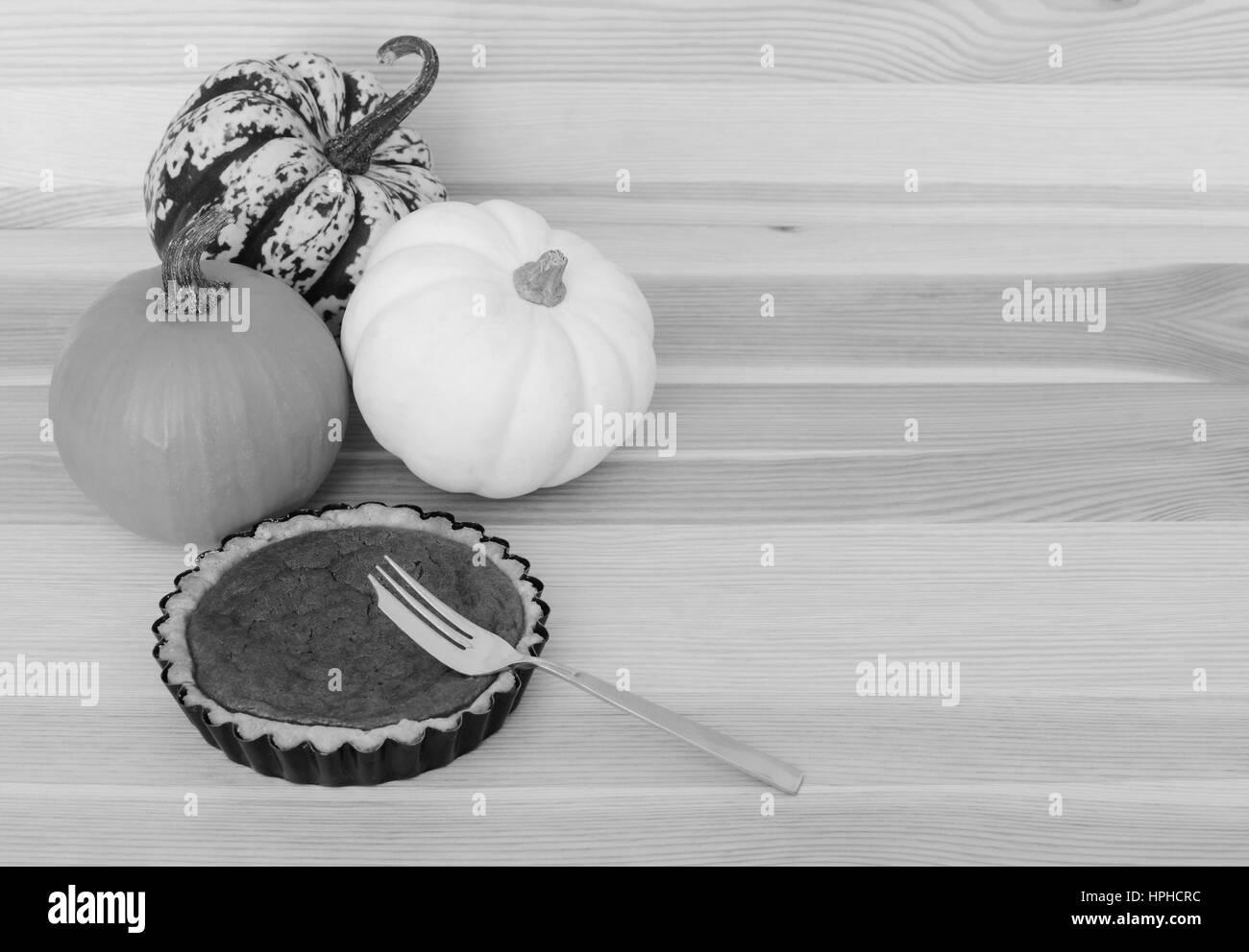Three mini pumpkins with small pumpkin pie and fork on a wooden table, with copy space Stock Photo