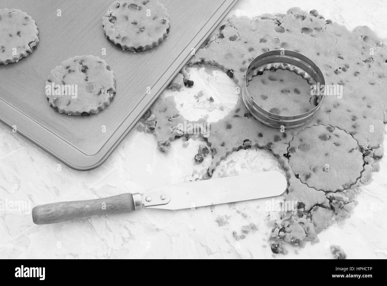 Baking chocolate chip cookies - cutting circles from dough with a cookie cutter. A palette knife is used to transfer the shapes to the baking tray. Stock Photo