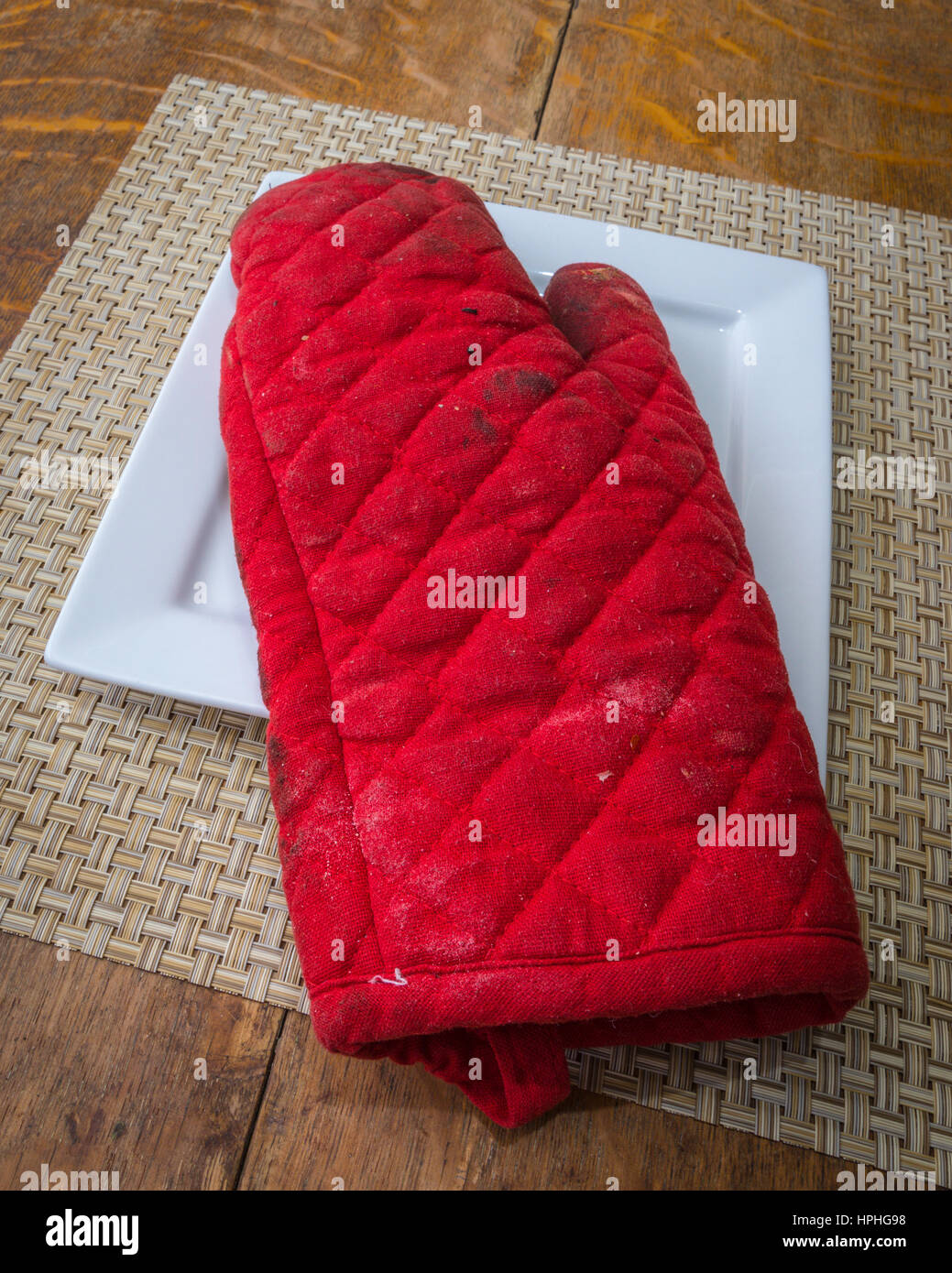 A well used red oven mitt on a white plate Stock Photo