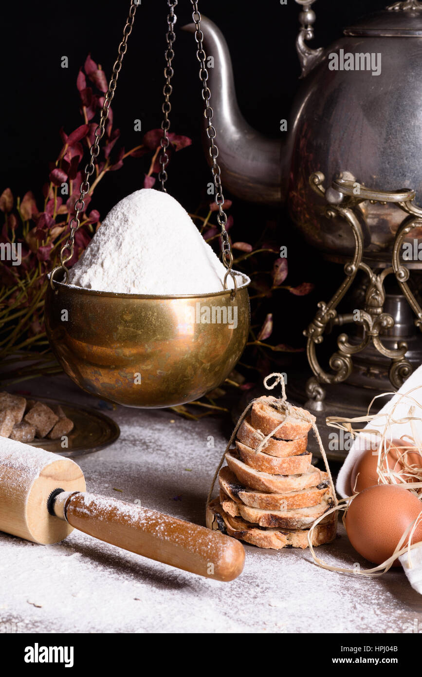 Bread baking ingredients - flour, eggs, baking powder. Baked flour-based food still life with antique teapot. Stock Photo