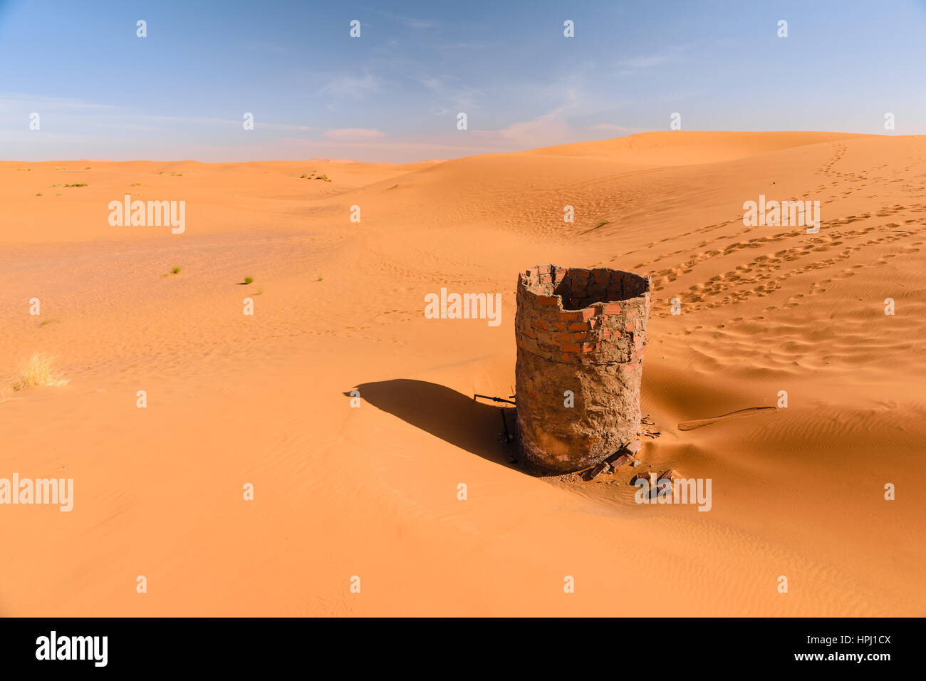 View over the dunes of Erg Chebbi desert near Merzouga in Morocco with a dry water well in the foreground. Stock Photo