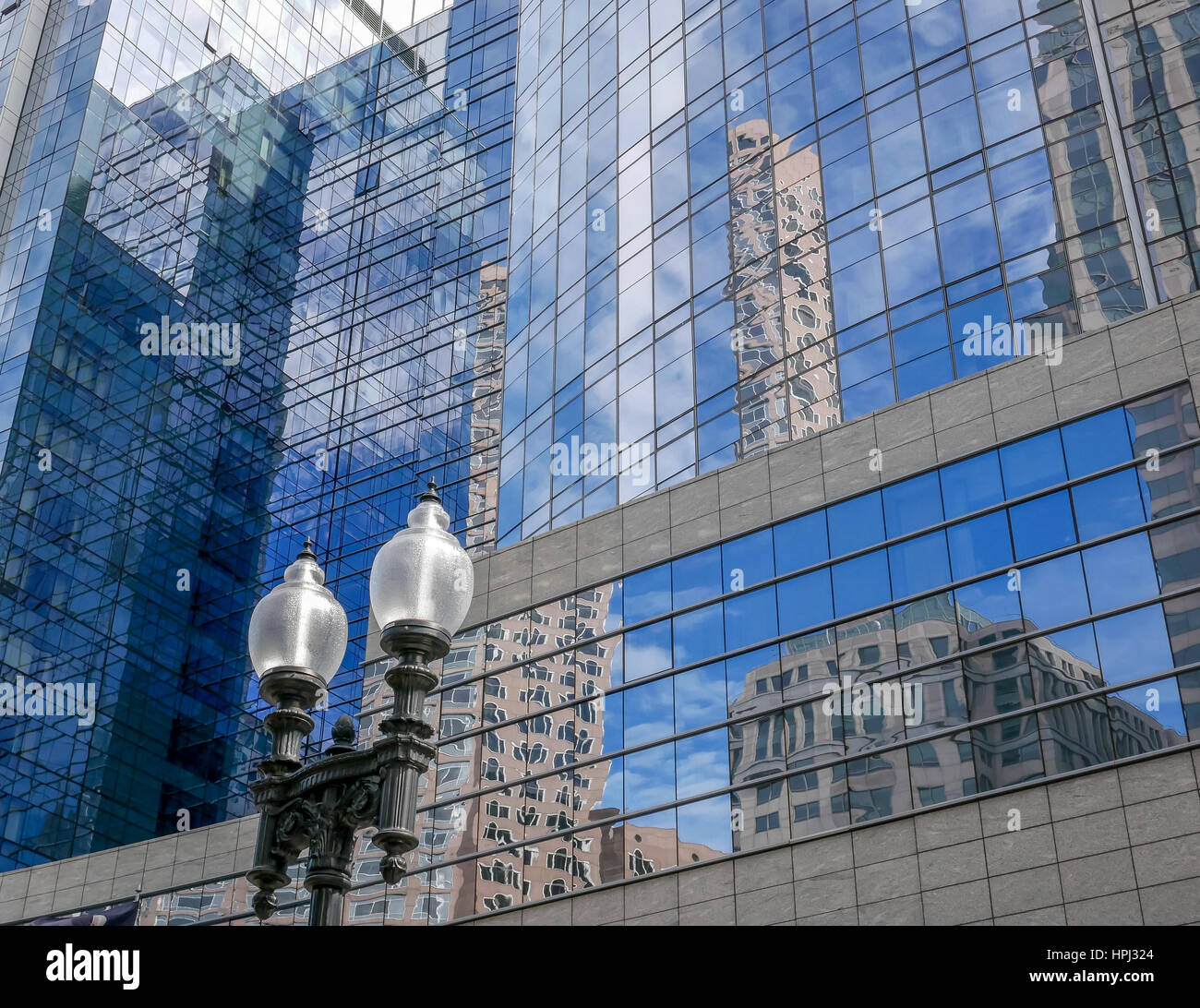 Looking skyward to Boston skyscrapers and blue sky reflected in glass facade of modern office building with old fashioned lamp post in foreground Stock Photo