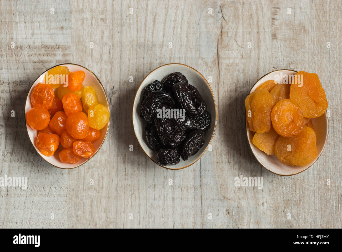 Three plates with dried fruits on wooden background dried mandarins, prunes and dried apricots