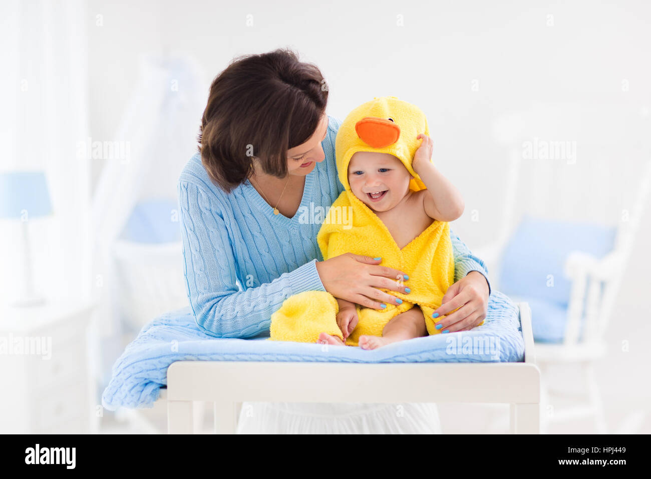 Mother and baby change diaper after bath in white nursery. Little boy