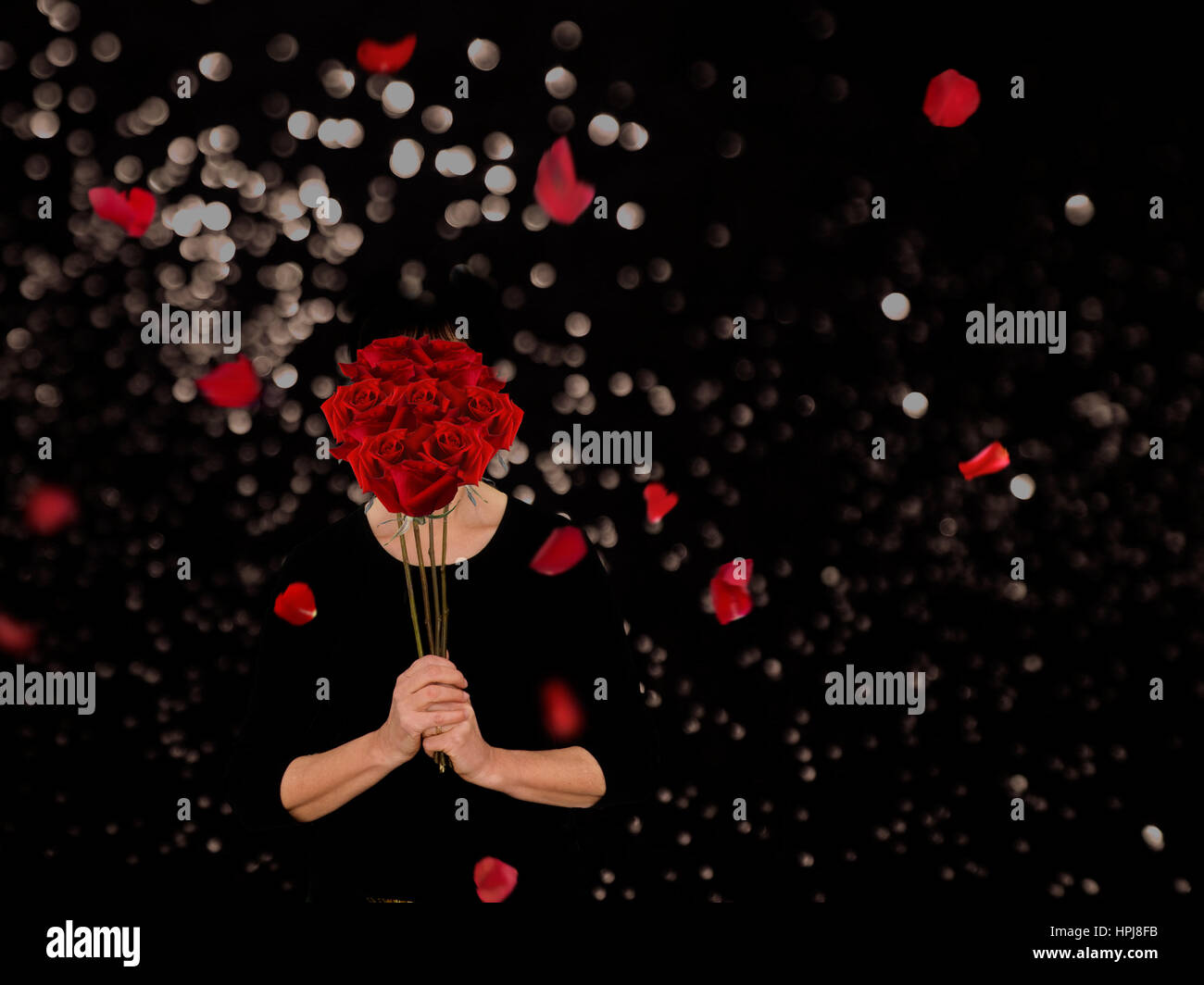Woman enjoying perfume of roses. Dramatic black background. Stock Photo