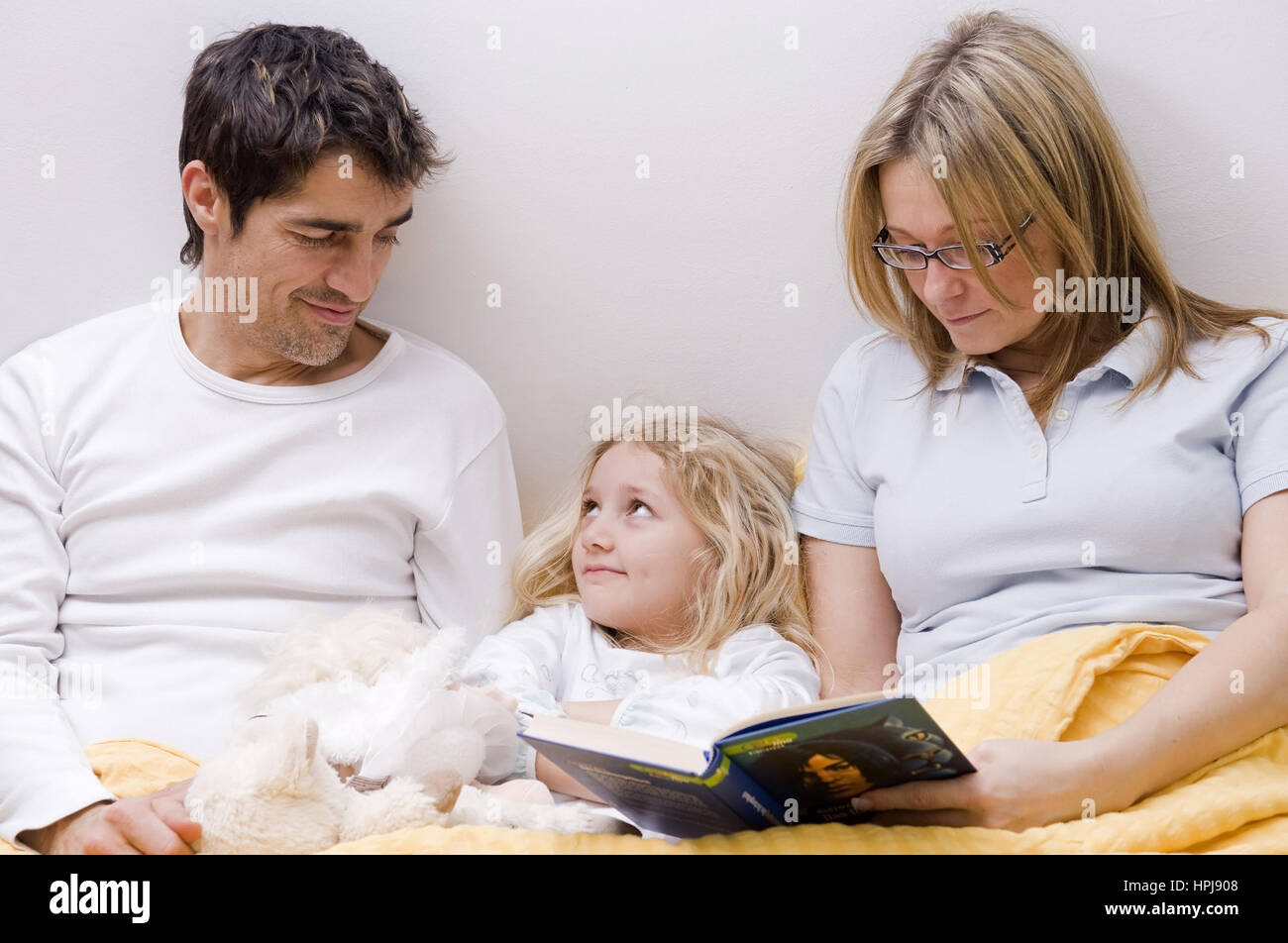 Model released , Eltern und Tochter gemeinsam im Bett, Mutter liest aus einem Buch vor - parents and daughter together in a bed Stock Photo