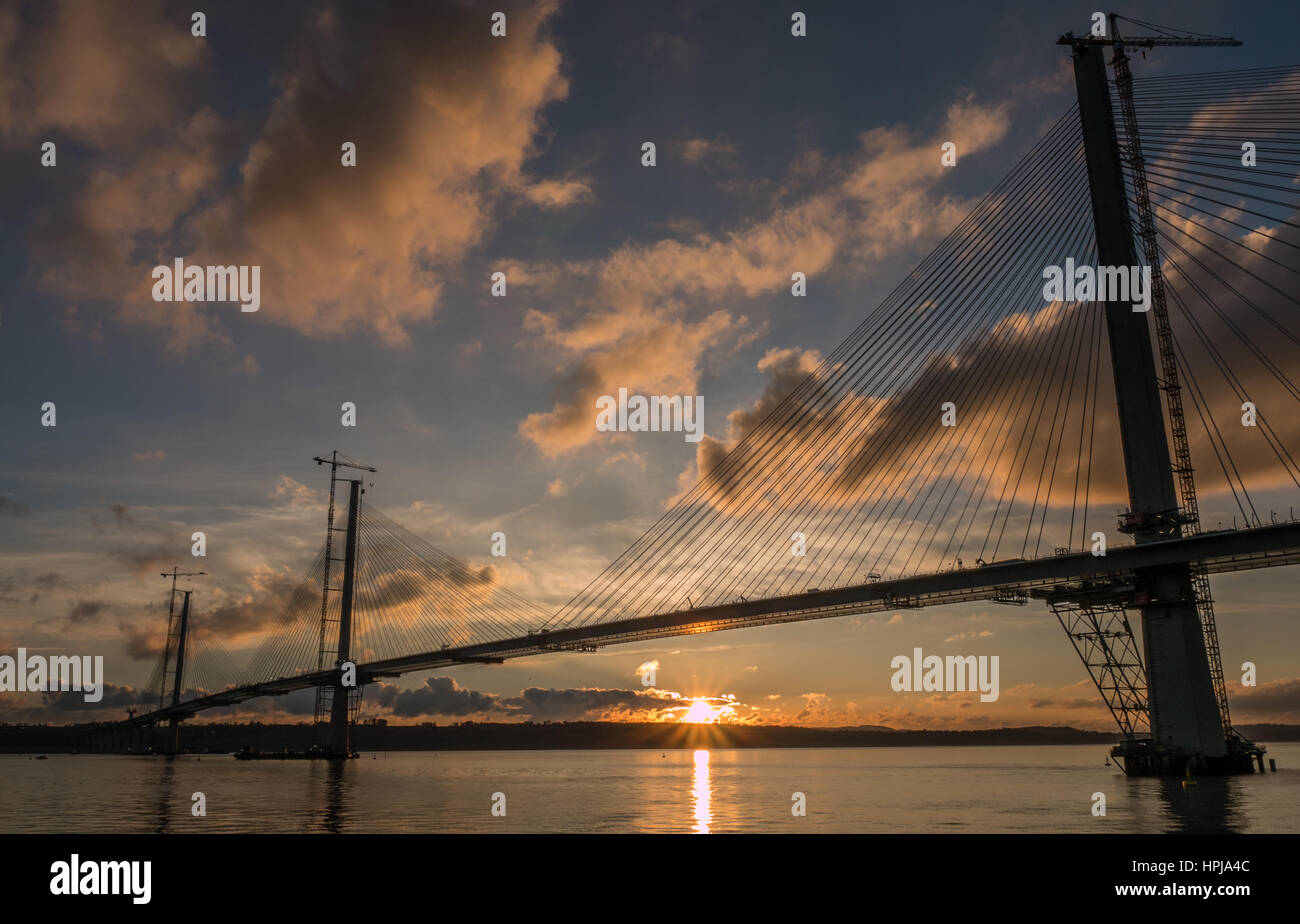 Sunset view with sun reflected in water over Queensferry Crossing under construction, Firth of Forth, Scotland, UK, from Fife side of Forth estuary Stock Photo